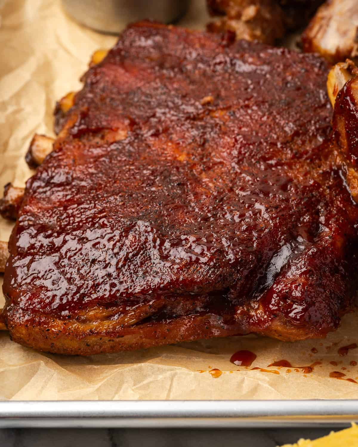 A rack of spareribs coated with BBQ sauce on a metal serving tray. 