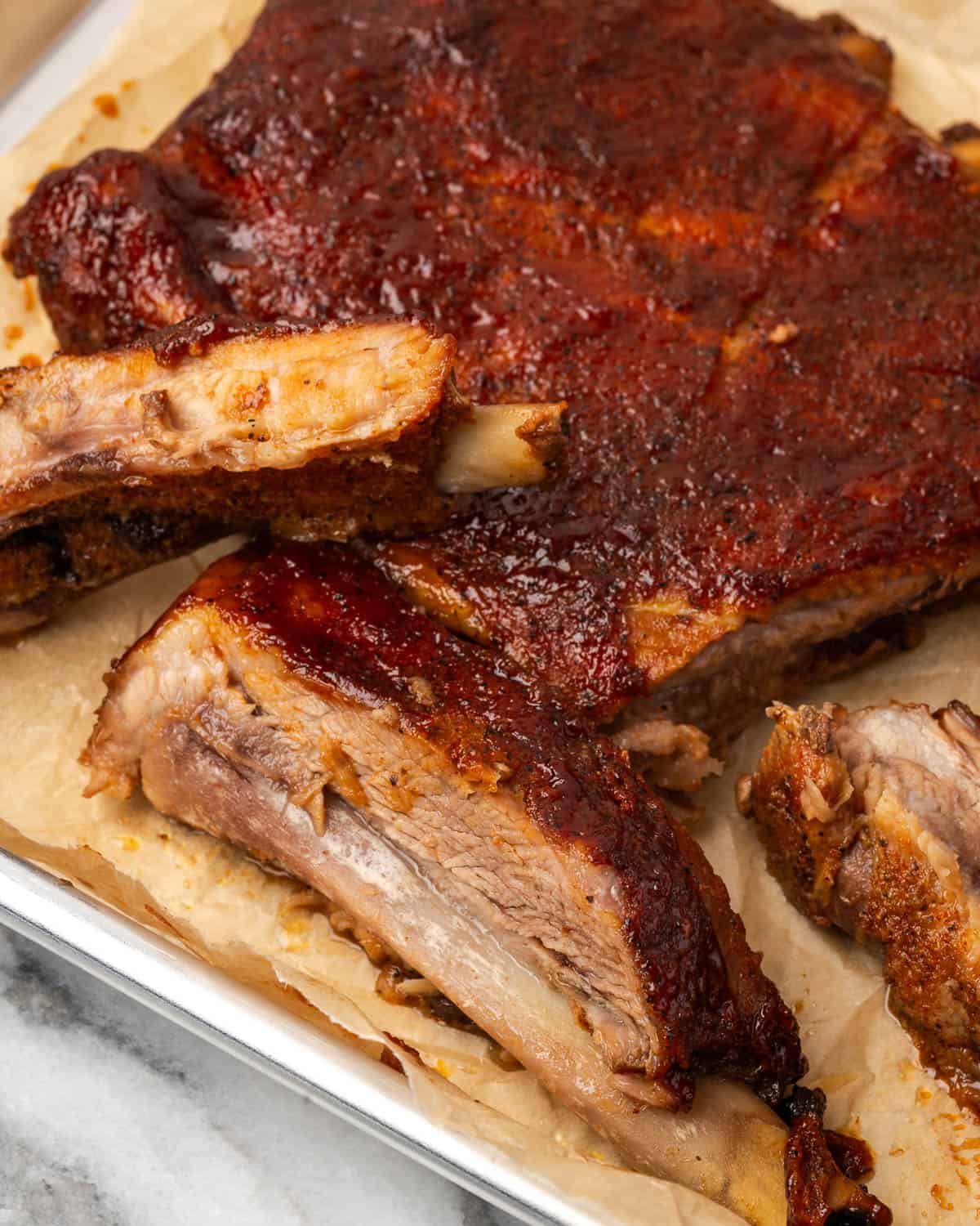 Several BBQ spareribs sliced and sitting on a metal serving tray.
