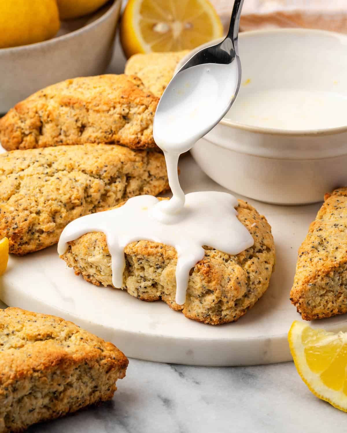 White icing being drizzled over freshly baked lemon poppy seed scones.