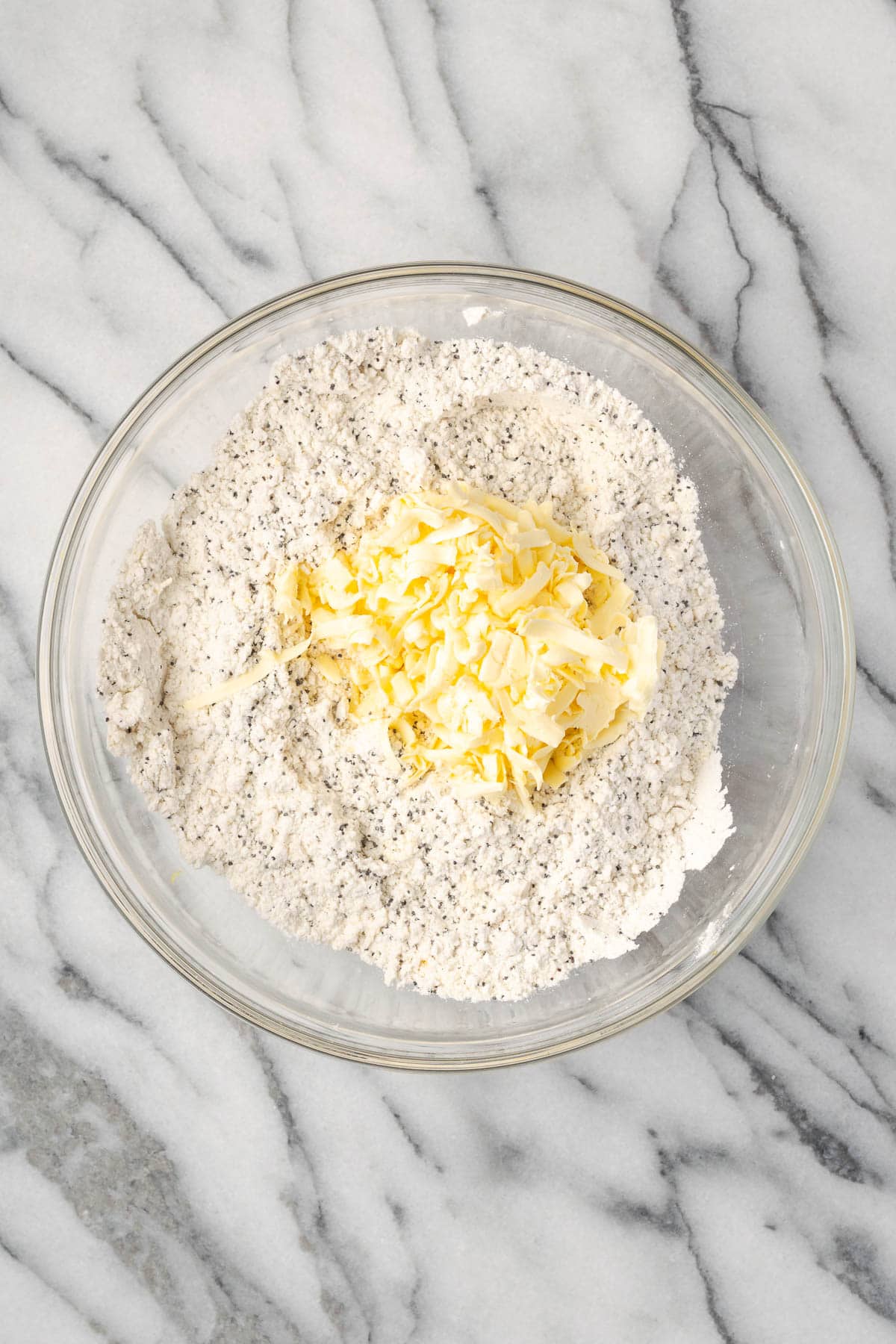 Grated butter being added into the bowl of dry ingredients.