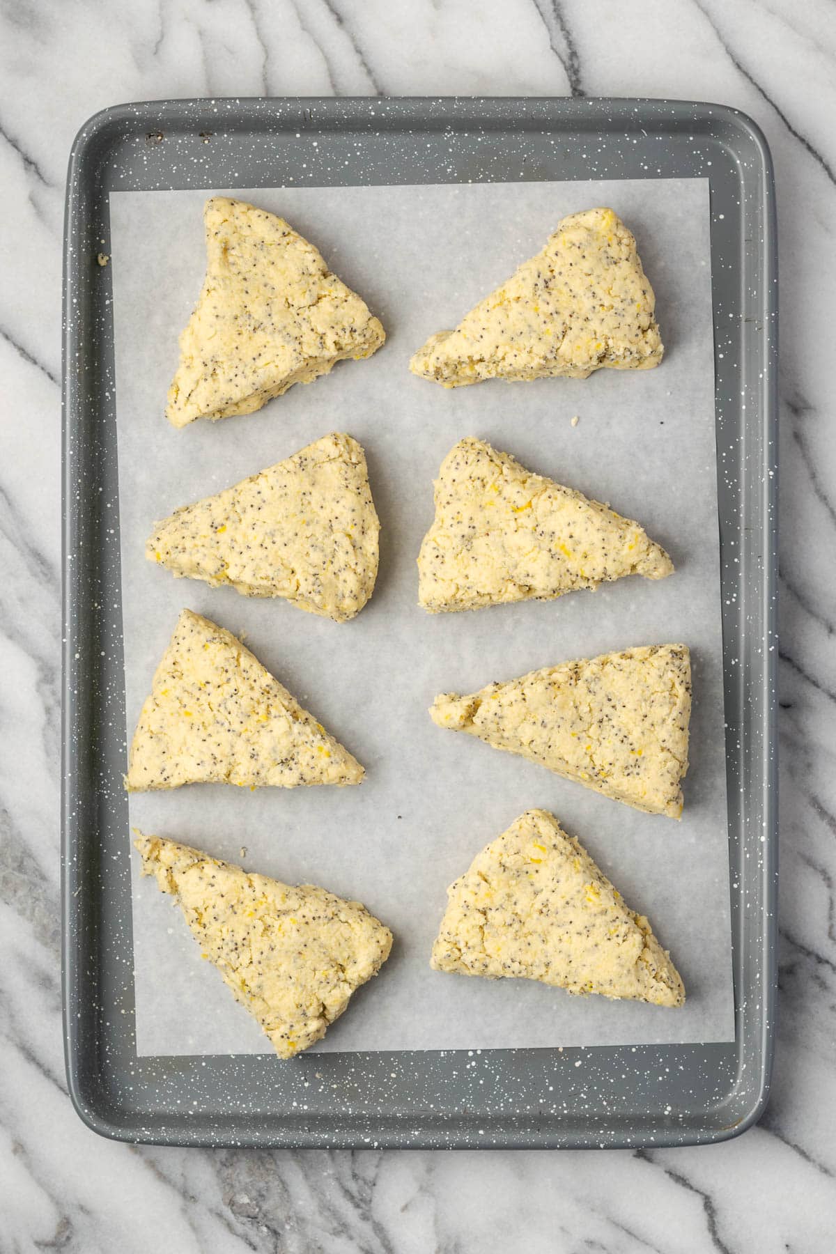 Eight unbaked lemon poppy seed scones on a baking sheet.