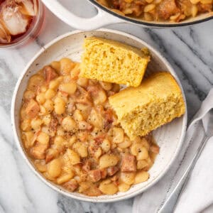 A bowl of lima beans and ham with two pieces of cornbread.