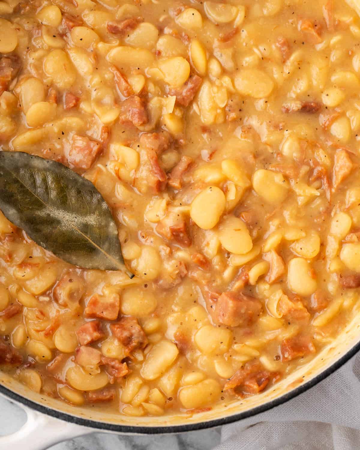 A pot of cooked lima beans with ham with a bay leaf on top. 