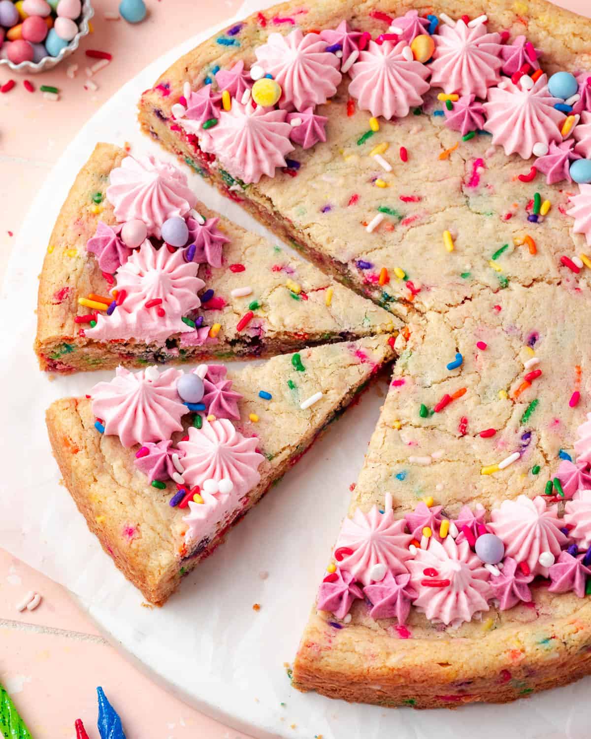 A sugar cookie cake decorated with pink frosting cut into wedges for serving.