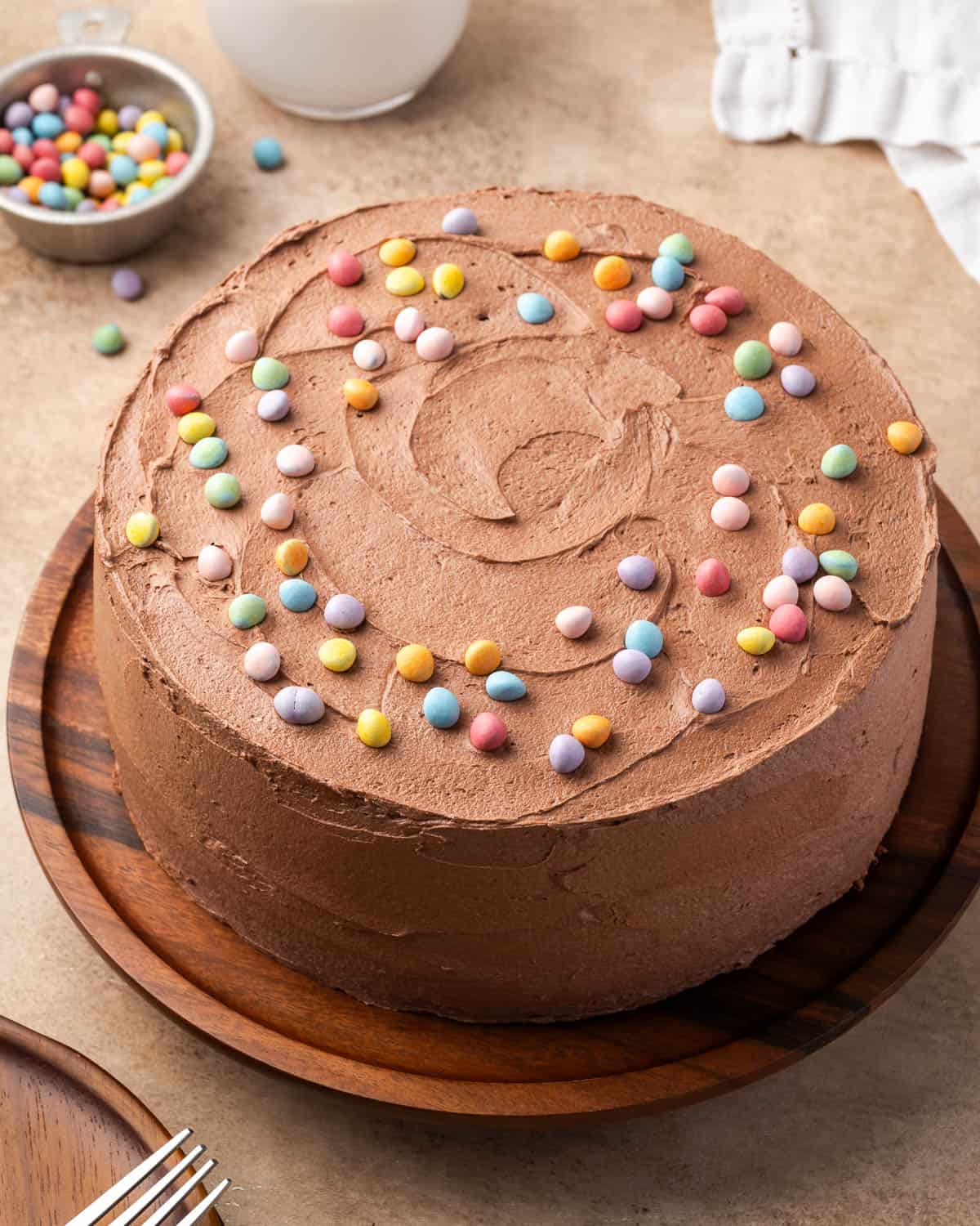 A decorated gluten free chocolate cake on a small wooden cake stand.