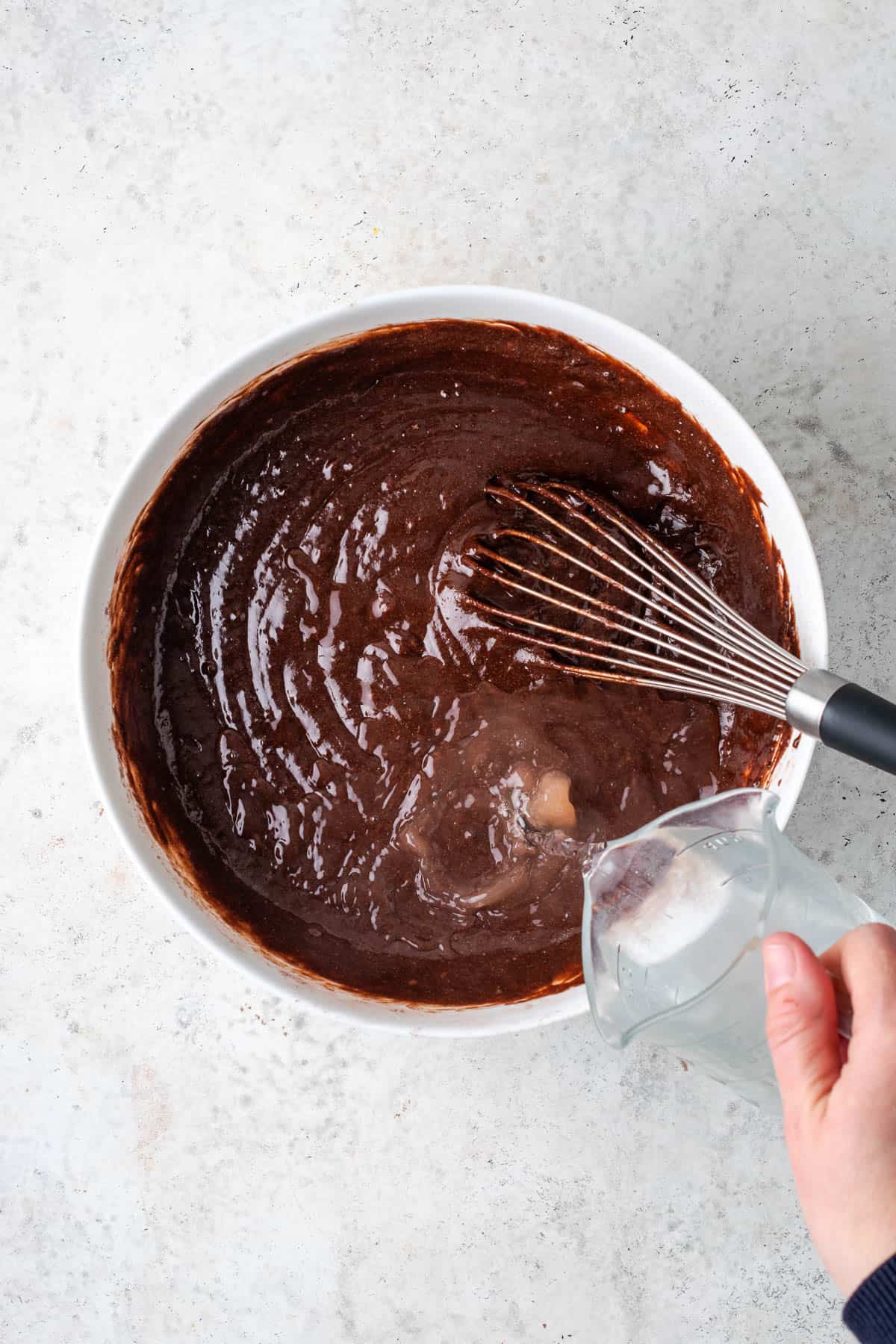Hot water being poured into the chocolate cake batter.