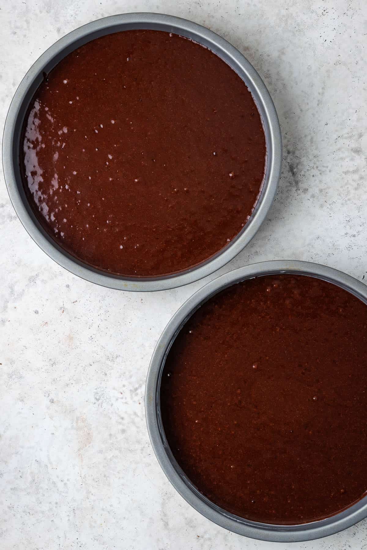 Cake batter divided into two round cake pans.