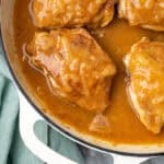Several chicken thighs covered with onion gravy in a cast iron pan.