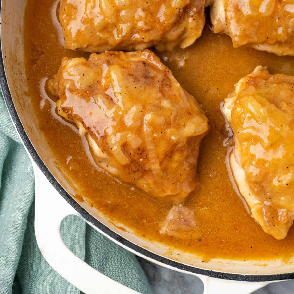 Several chicken thighs covered with onion gravy in a cast iron pan.