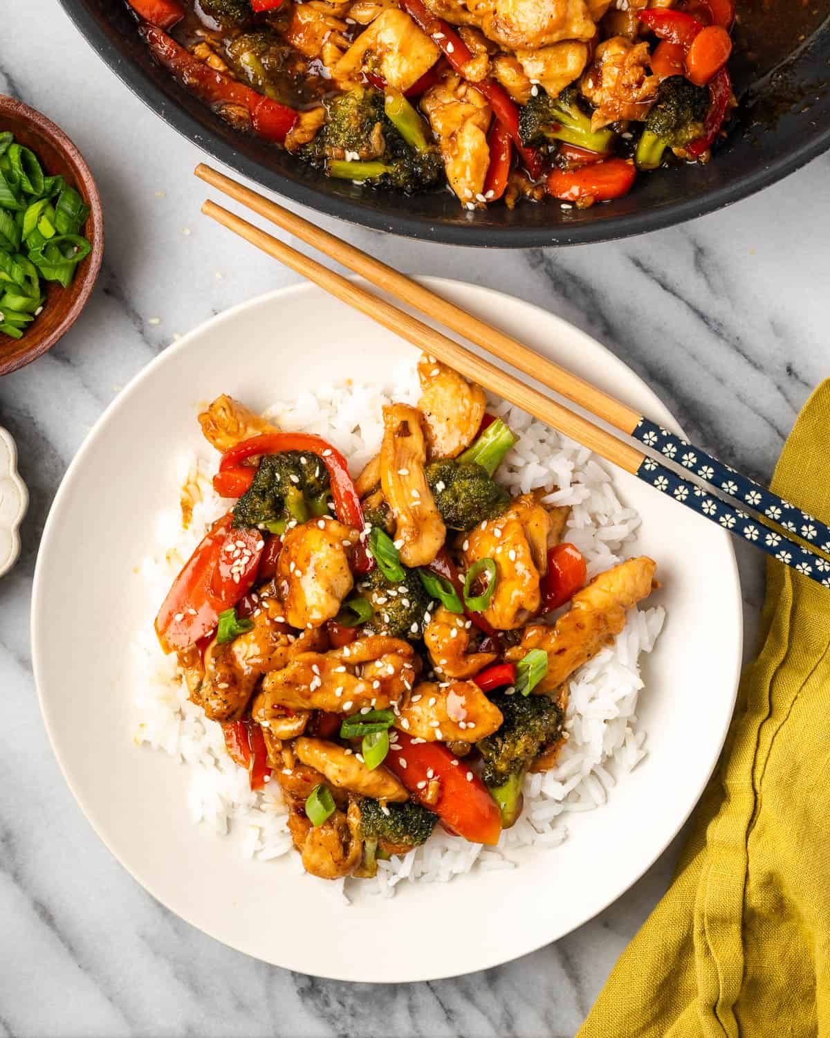 A teriyaki chicken rice bowl sitting on a marble counter next to a large skillet. 