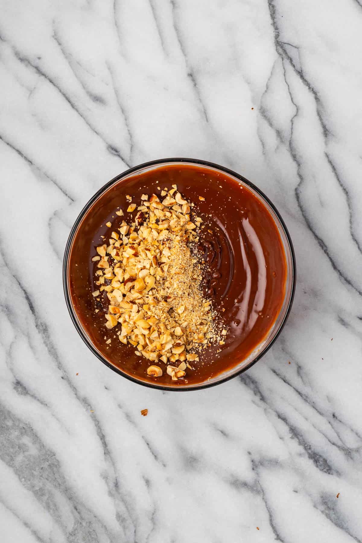 Chopped hazelnuts being stirred into chocolate ganache.