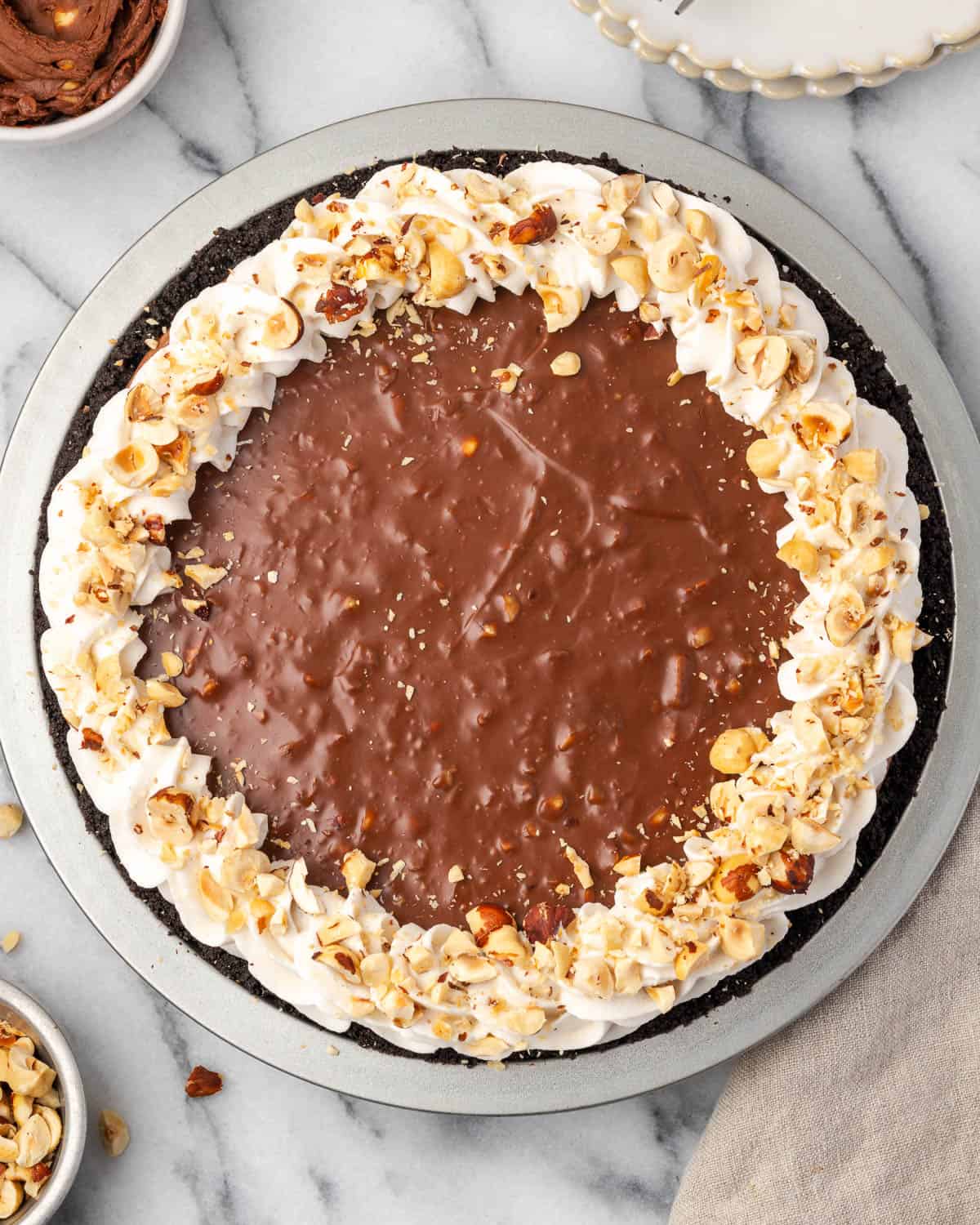 A Nutella pie topped with chocolate ganache, hazelnut whipped cream and chopped hazelnuts.