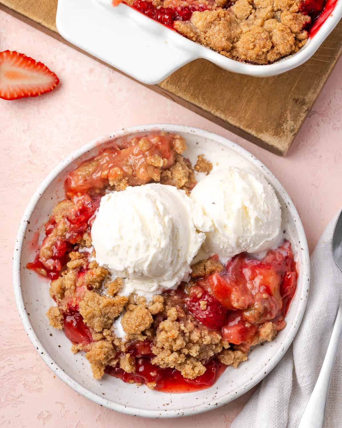 A dish of strawberry rhubarb crumble topped with two scoops of vanilla ice cream.