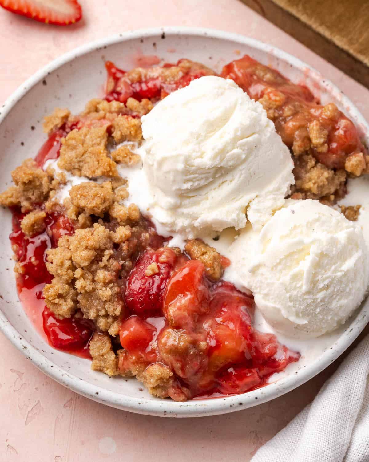 Strawberry rhubarb crumble topped with vanilla ice cream served on a small dessert plate.