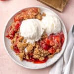 Strawberry rhubarb crumble topped with ice cream on a small dessert plate.