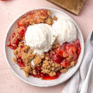 Strawberry rhubarb crumble topped with ice cream on a small dessert plate.