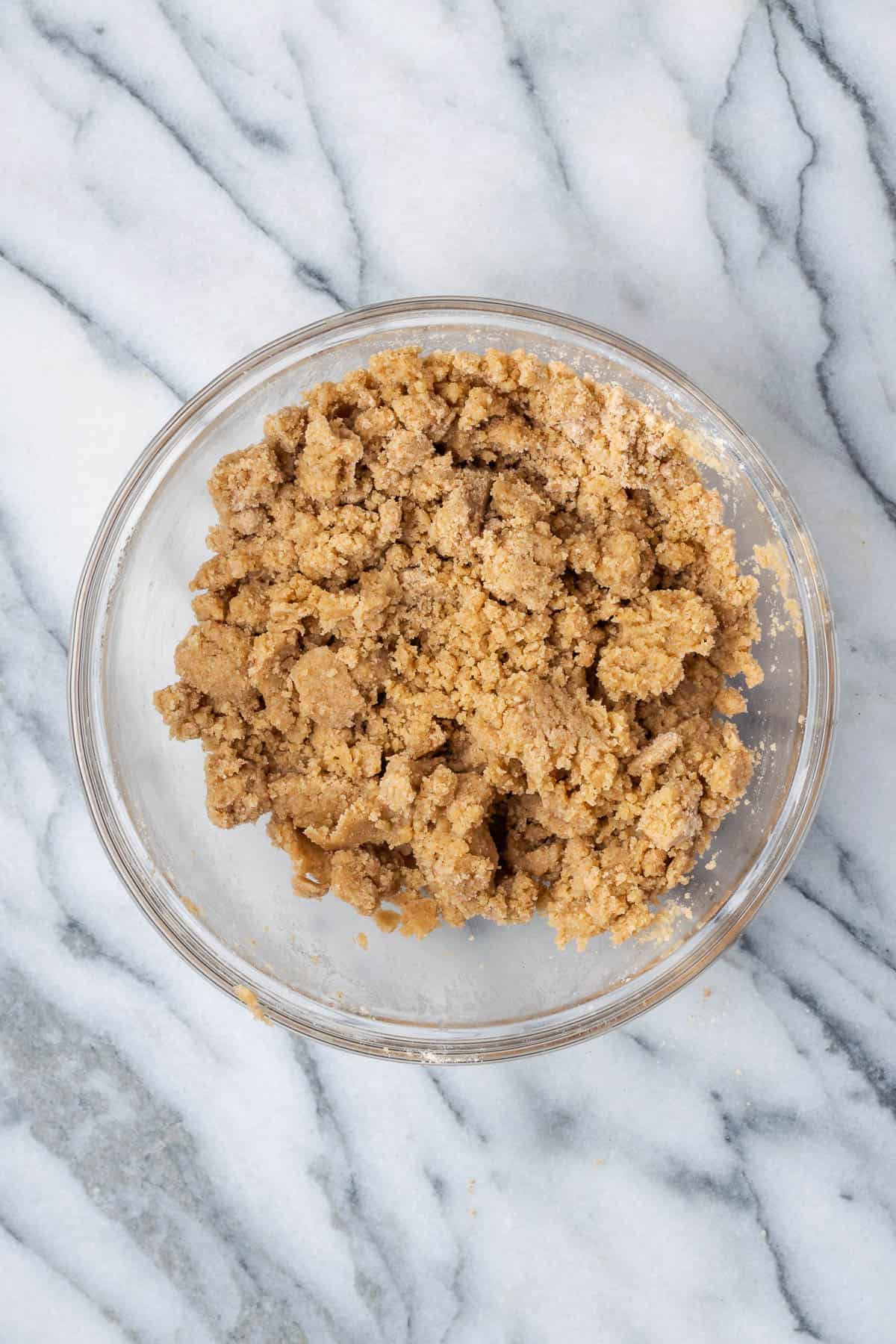 A bowl of crumble topping sitting on a marble counter.