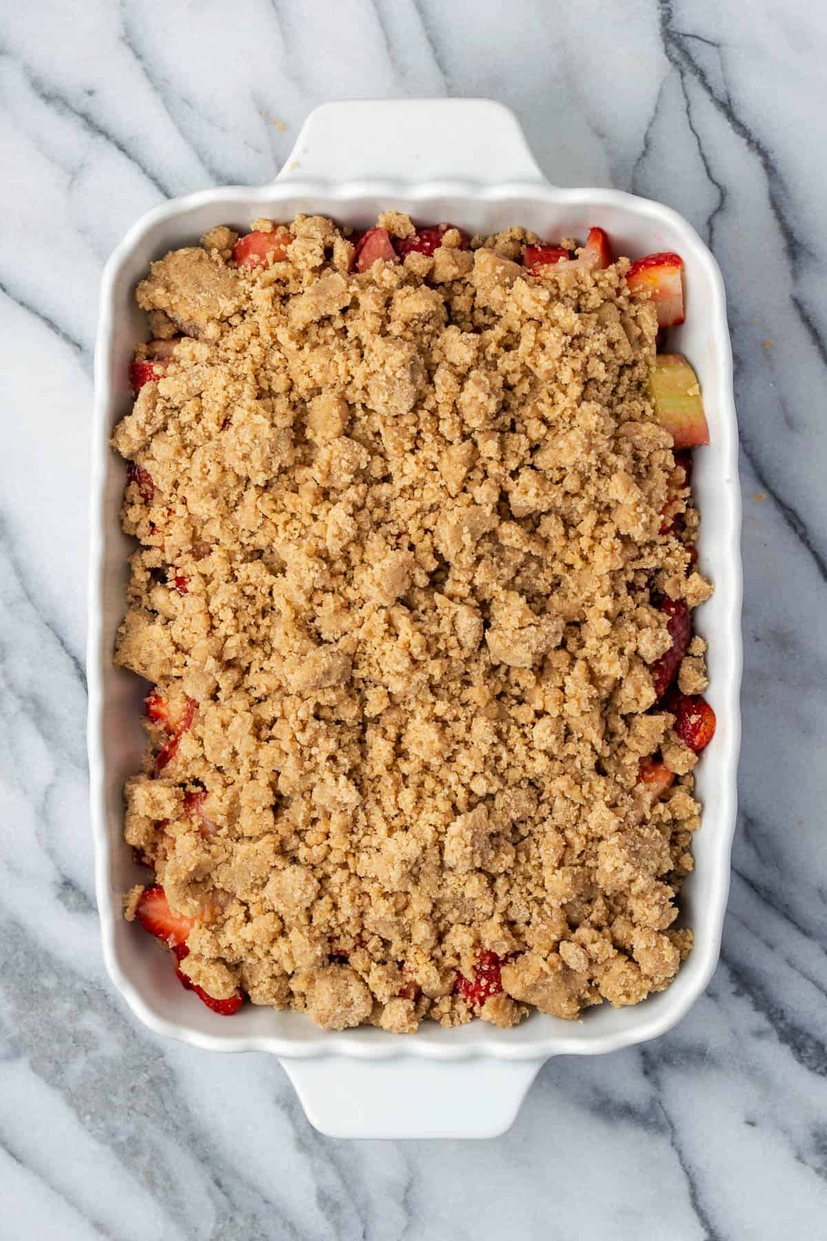 An unbaked strawberry rhubarb crumble sitting on a marble counter.
