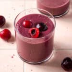 A cherry smoothie served in a small glass sitting on a tile counter.