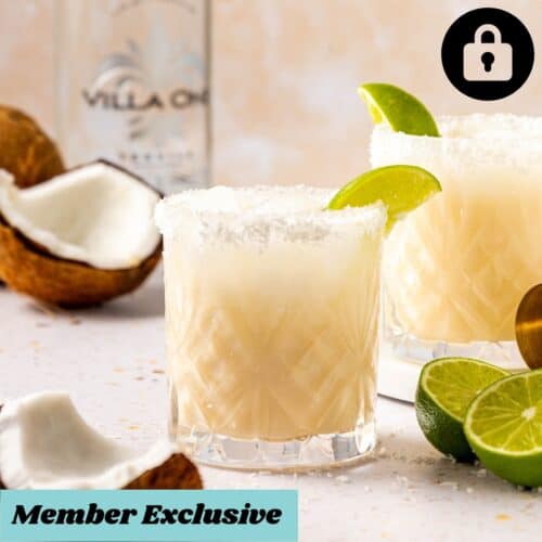 Two glasses of coconut lime margarita sitting next to a bottle of tequila.