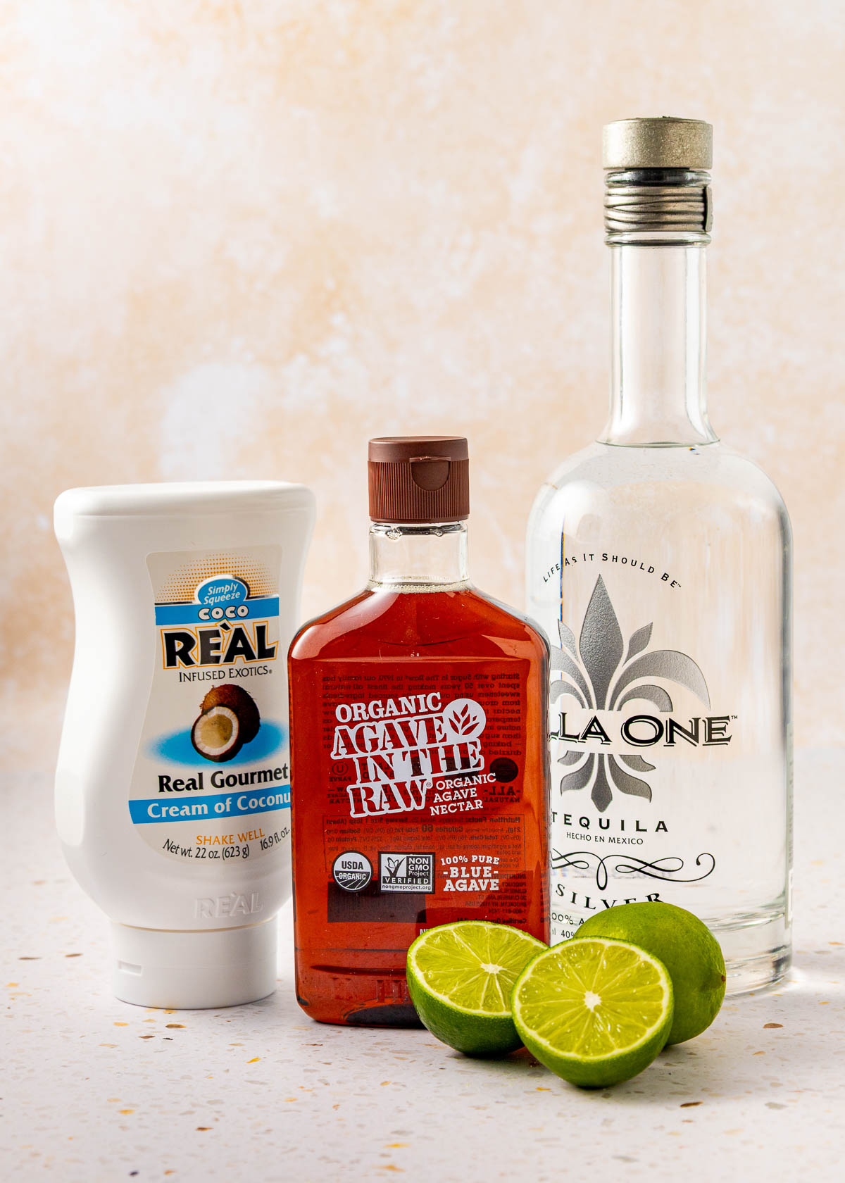 Ingredients for a coconut lime margarita sitting on a white counter.