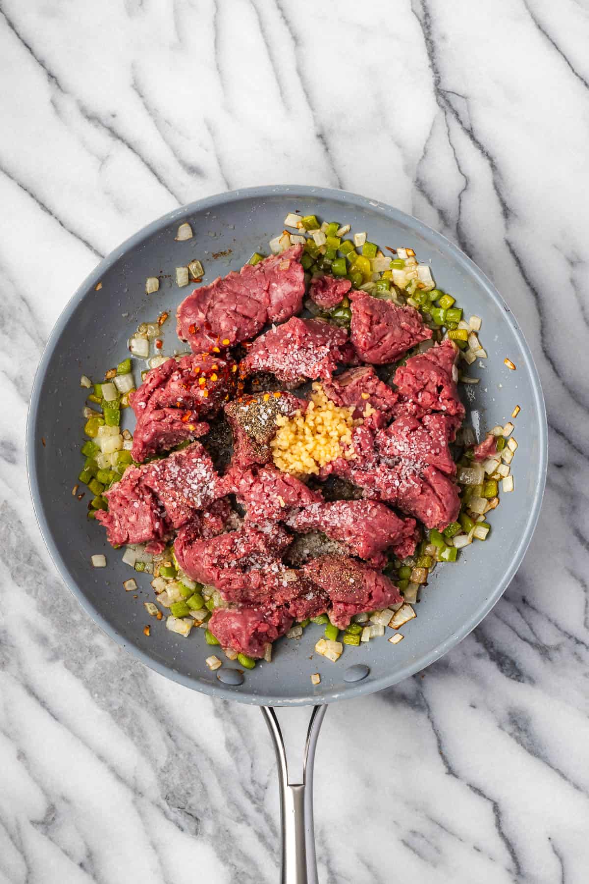 Ground beef, minced garlic, and seasonings added to the skillet with the sauteed vegetables.