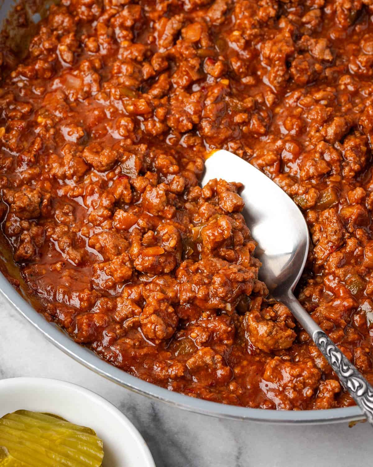 A spoon scooping into a pan of sloppy joe meat.