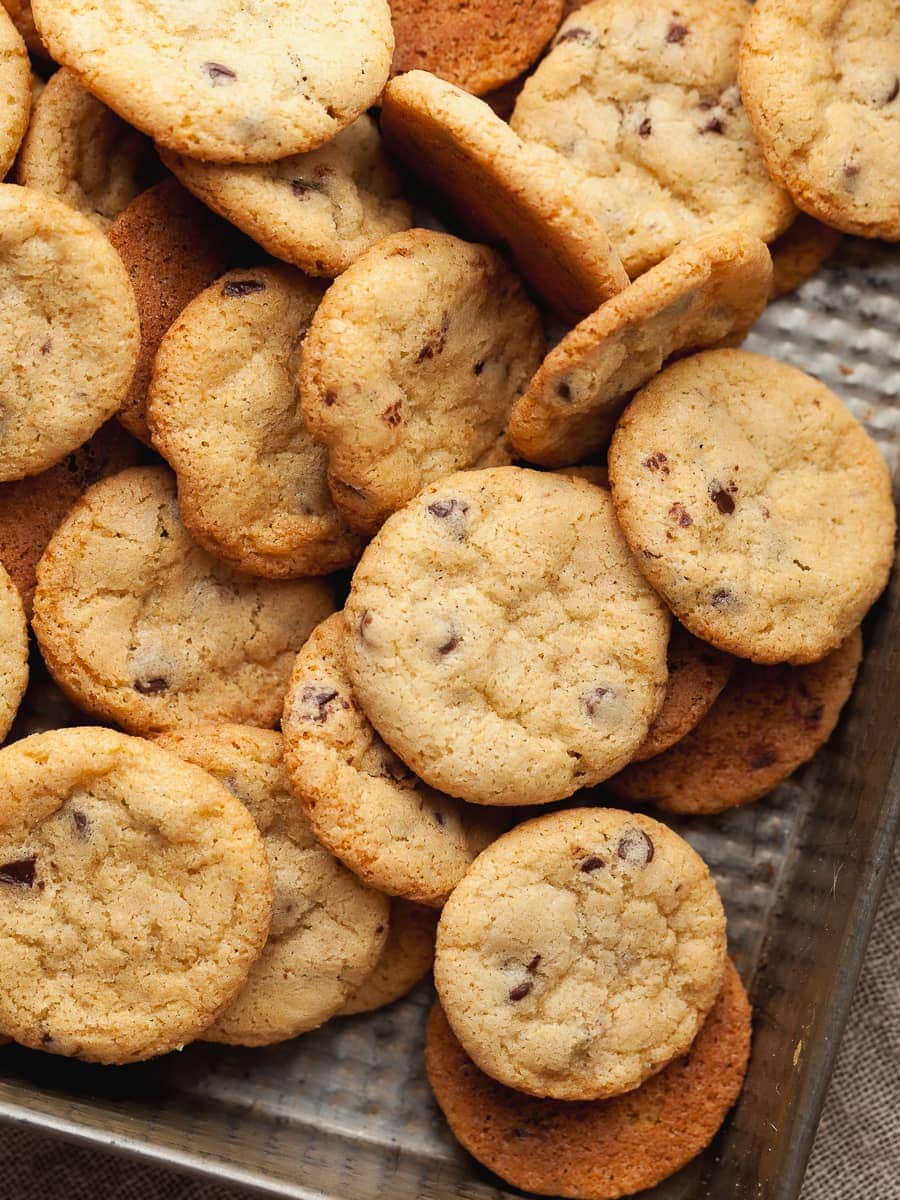 Mini chocolate chip cookies scattered on a baking sheet.