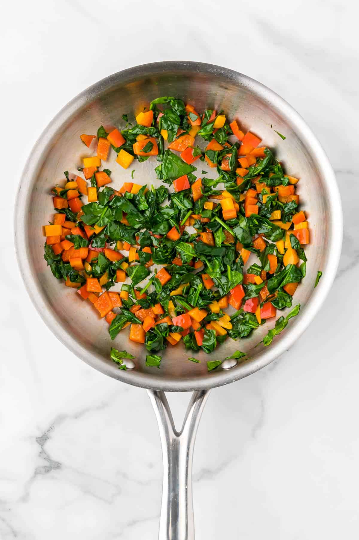 Red bell pepper and baby spinach being sauteed in a large cast iron skillet.
