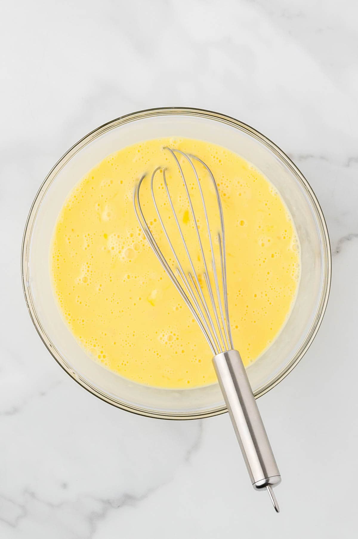 Eggs and milk whisked together in a large glass bowl.