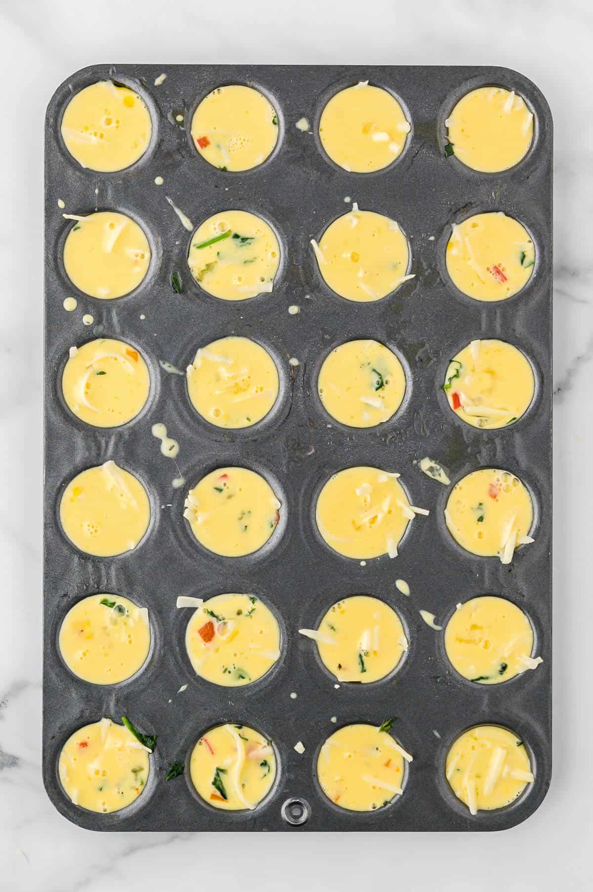 Egg mixture poured over the vegetables in a mini muffin tin. 