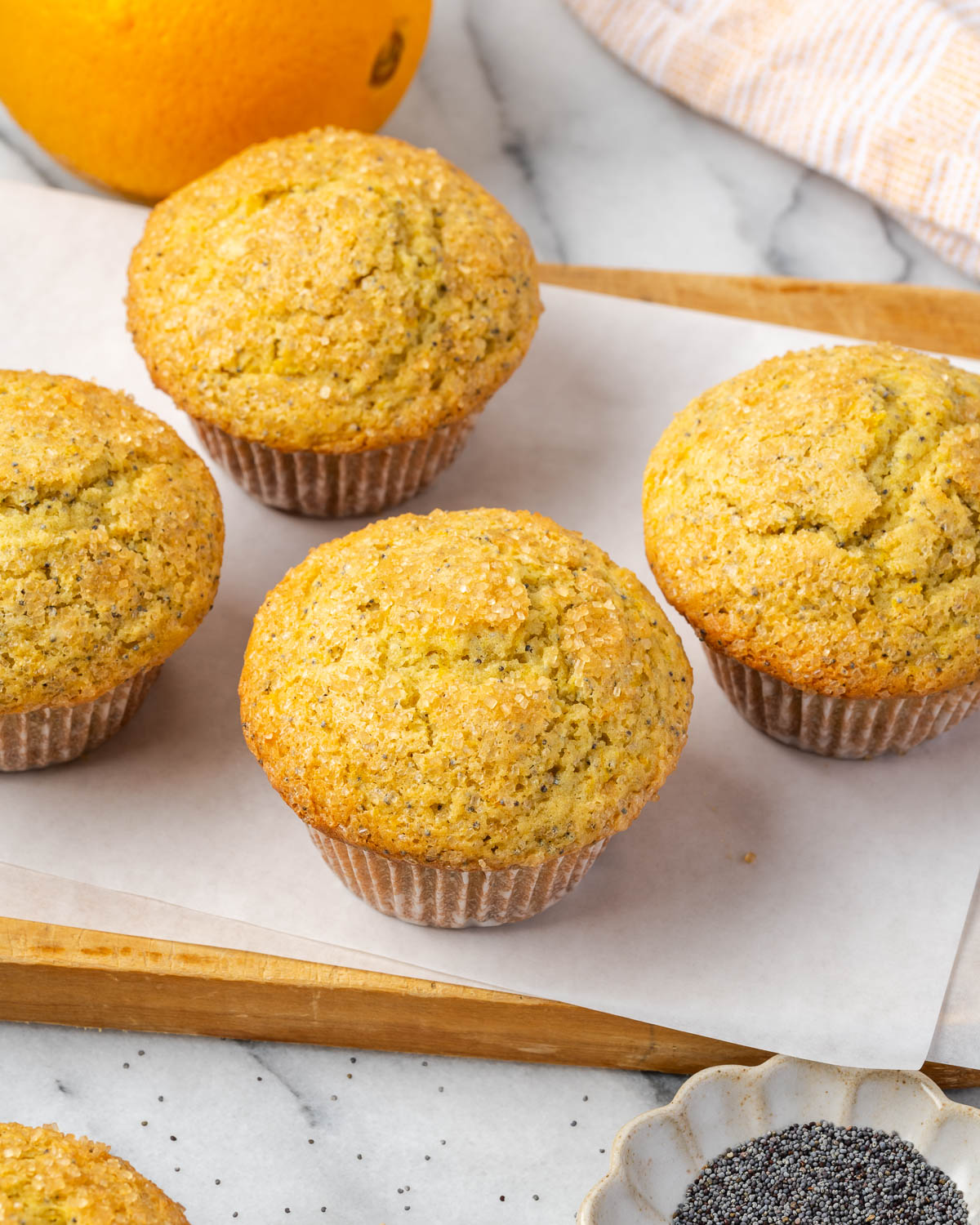 Several orange poppy seed muffins sitting on a wood cutting board.