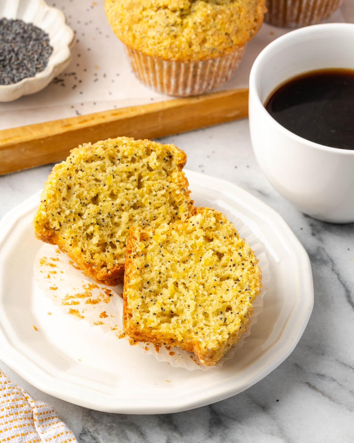 A muffin cut in half sitting on a small plate next to a cup of coffee.