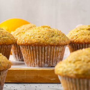 A batch of gluten free orange poppy seed muffins sitting on a wood cutting board.