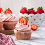 A strawberry cupcake decorated with pink frosting sitting on a marble counter.
