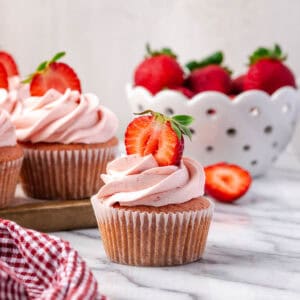 A strawberry cupcake decorated with pink frosting sitting on a marble counter.