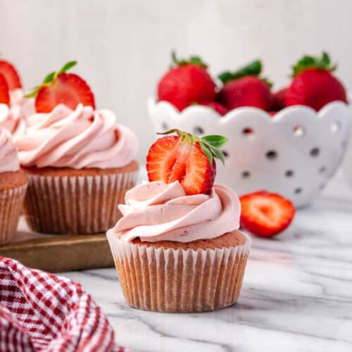 A strawberry cupcake decorated with pink frosting sitting on a marble counter.
