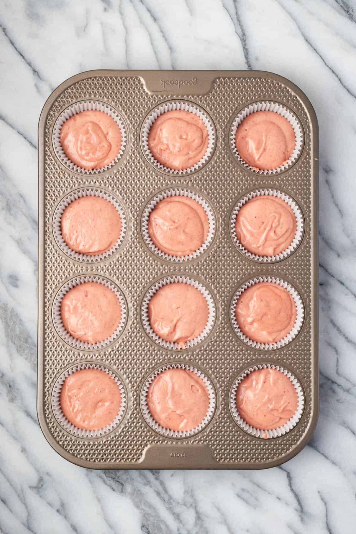 Strawberry cupcake batter portioned into a 12-cup muffin tin.