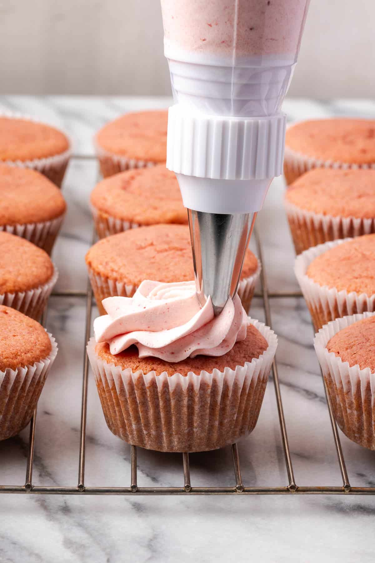 Strawberry buttercream frosting being piped onto strawberry cupcakes.