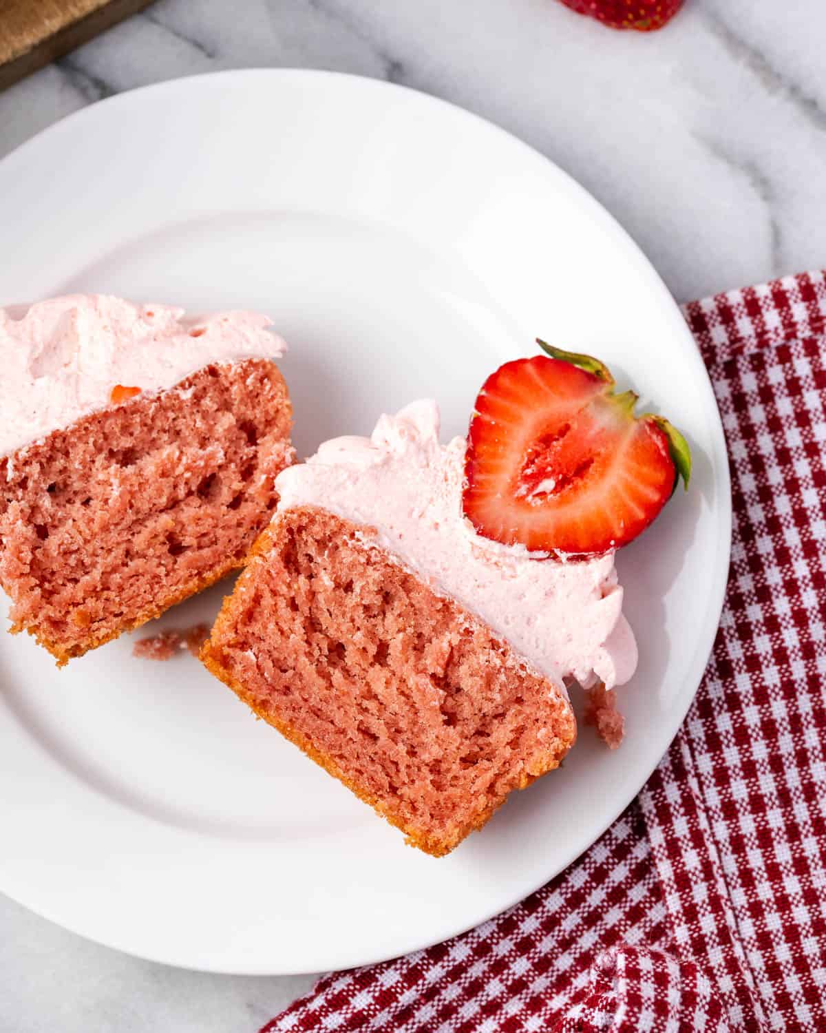 A strawberry cupcake cut in half sitting on a small dessert plate.