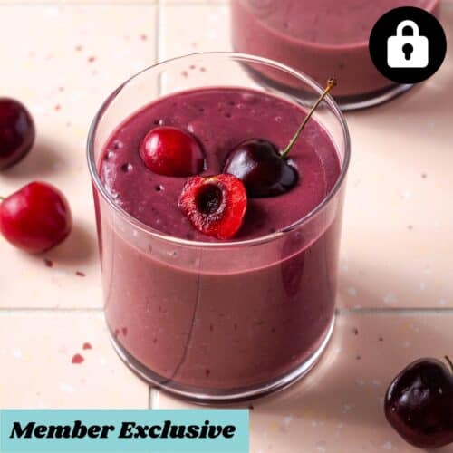 A cherry smoothie served in a short glass and topped with fresh cherries.