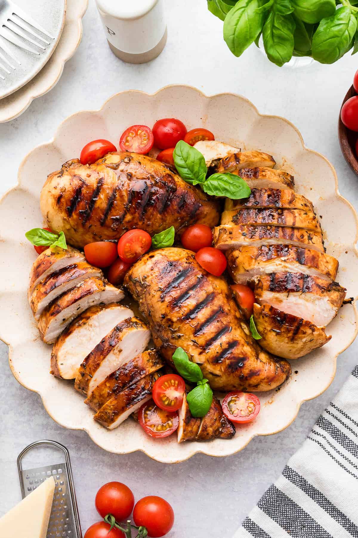 Several pieces of balsamic chicken on a serving plate with fresh basil and cherry tomatoes.
